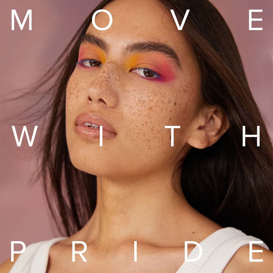 A woman wearing orange, yellow, and pink eyeshadow in a close up image of her face with the phrase “move with pride” over the top.  