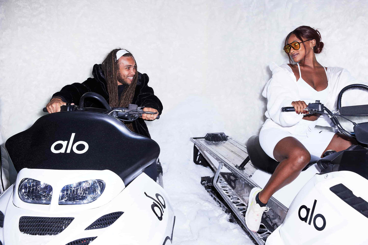 Clinton Moxam and Uche Nwosu posing on Alo branded snow mobiles at Alo Winter House 2021 wearing Alo faux fur jackets.  