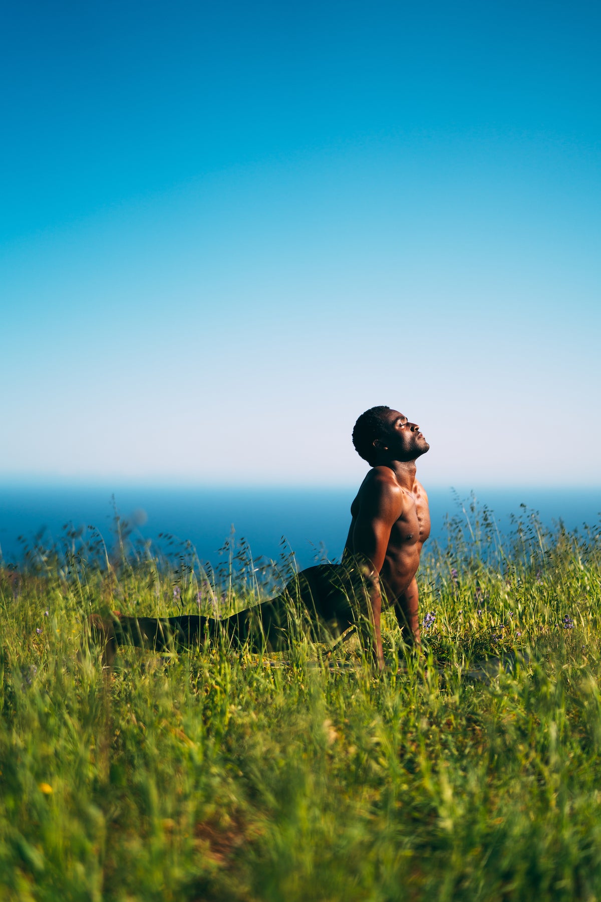Man performing Upward Dog while in tall grass overlooking the ocean.  