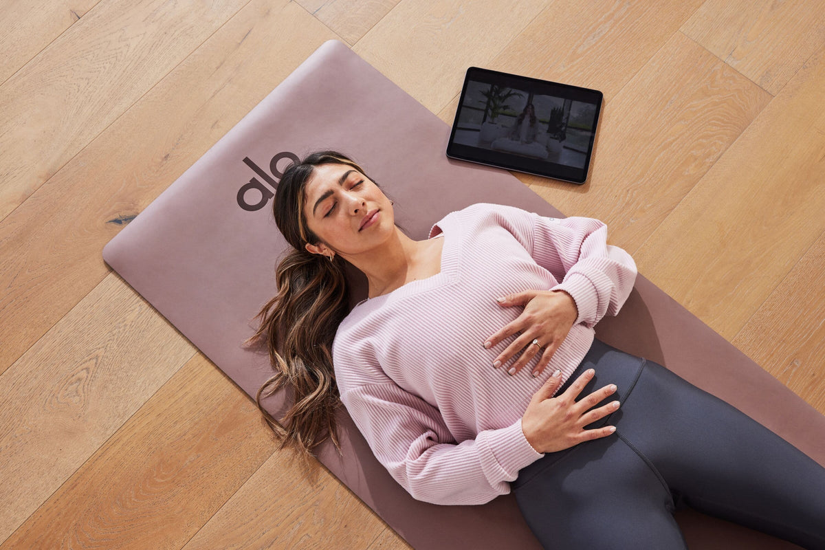 A woman meditating on a Warrior Mat using the Alo Moves online platform.  