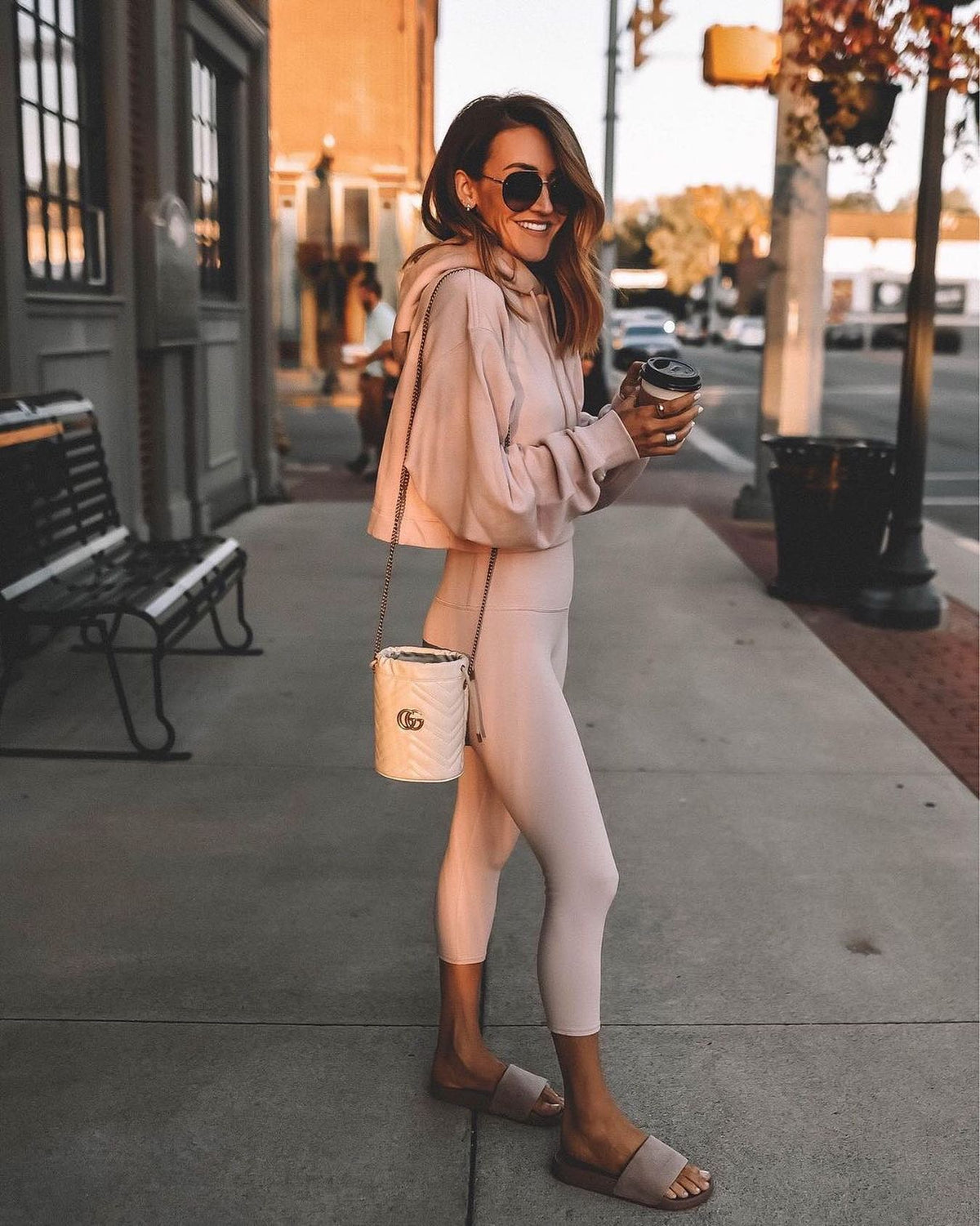 @karinastylediaries wearing a light pink capri legging with matched cropped sweatshirt with slides, a designer purse, and sunglasses while grabbing a coffee. 