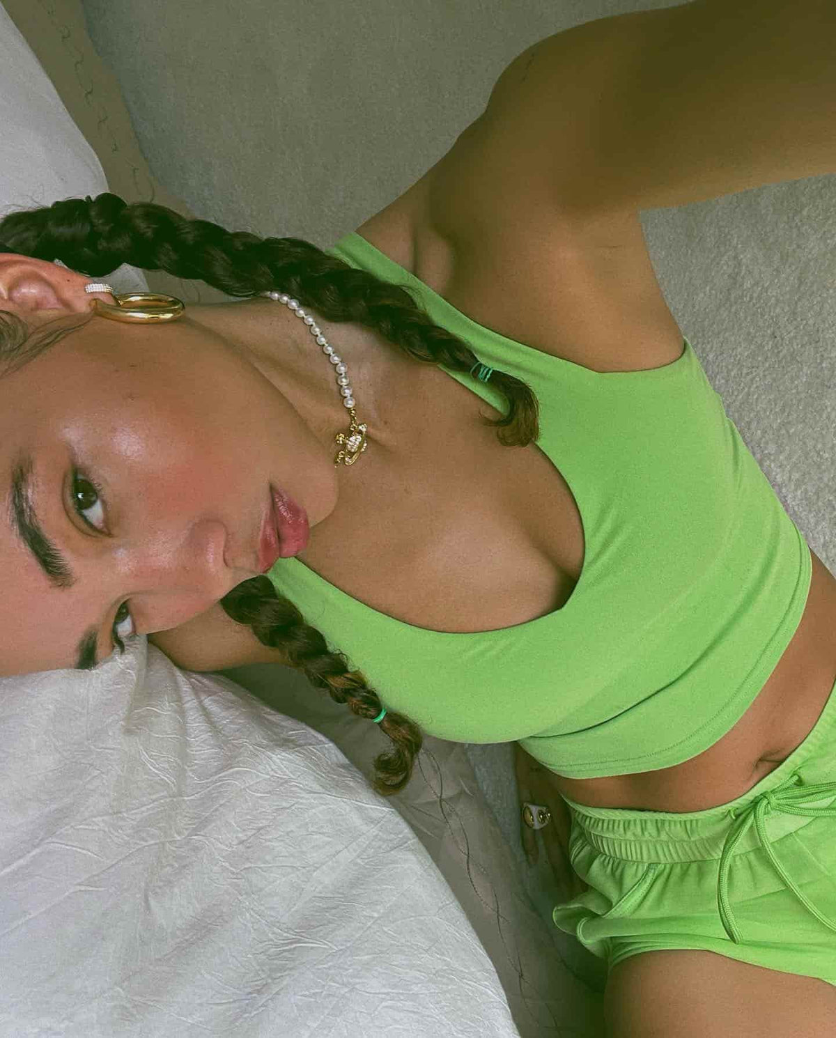 Ashley Moore wearing the Real Bra Tank in Green Apple with matching running shorts while taking a selfie on her bed.  