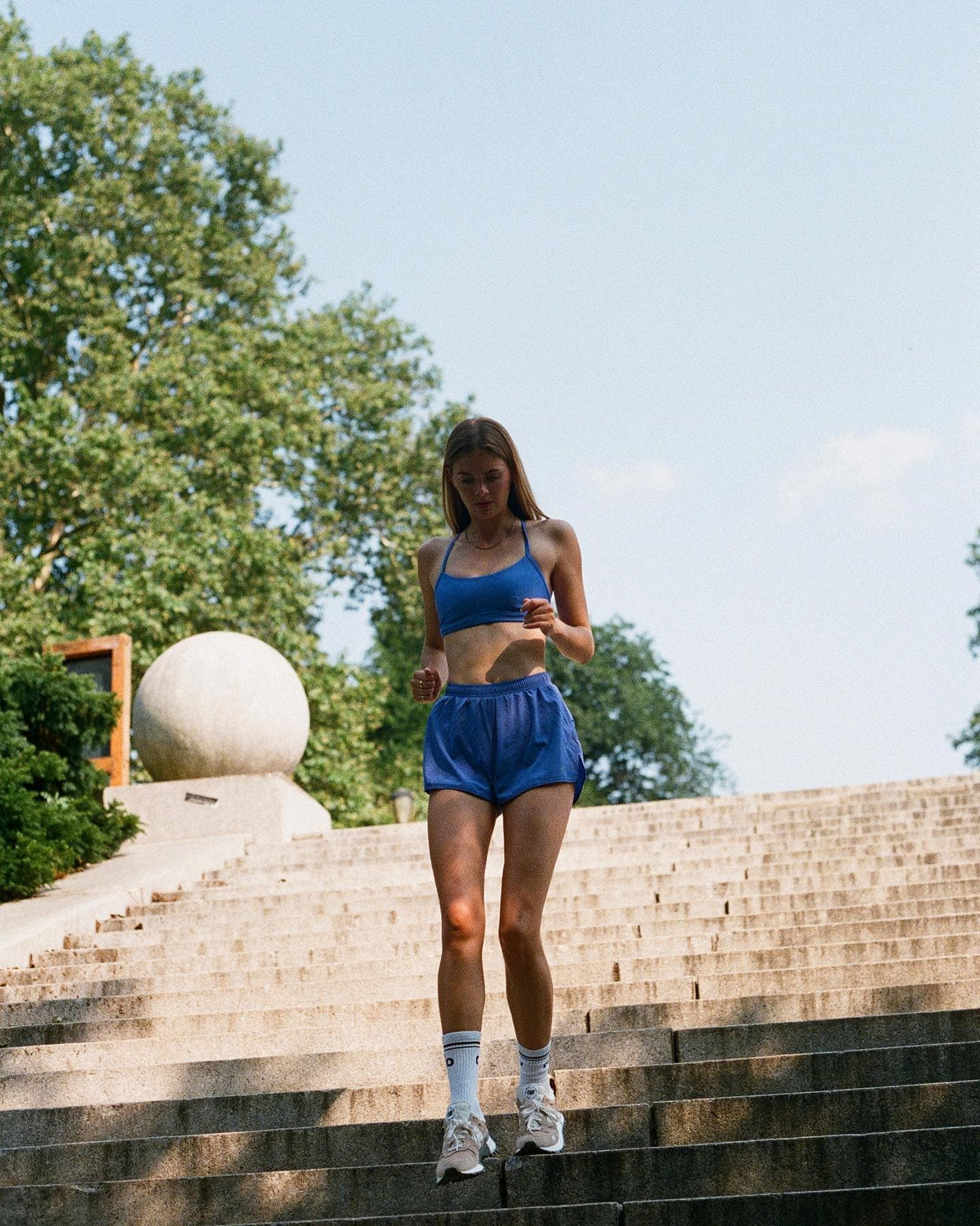 @meganmayw wearing a pair of Alo Blue Stride Shorts with a matching Airlift Intrigue Bra while running staircases at a local public park. 