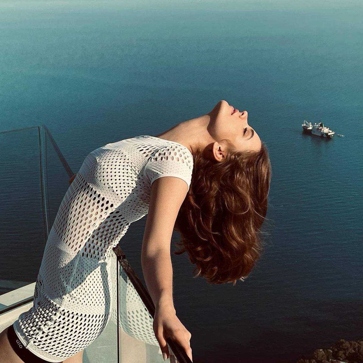 @realbarbarapalvin wearing a Mesh Haute Summer Dress in White while leaning over a balcony overlooking a large body of water. 