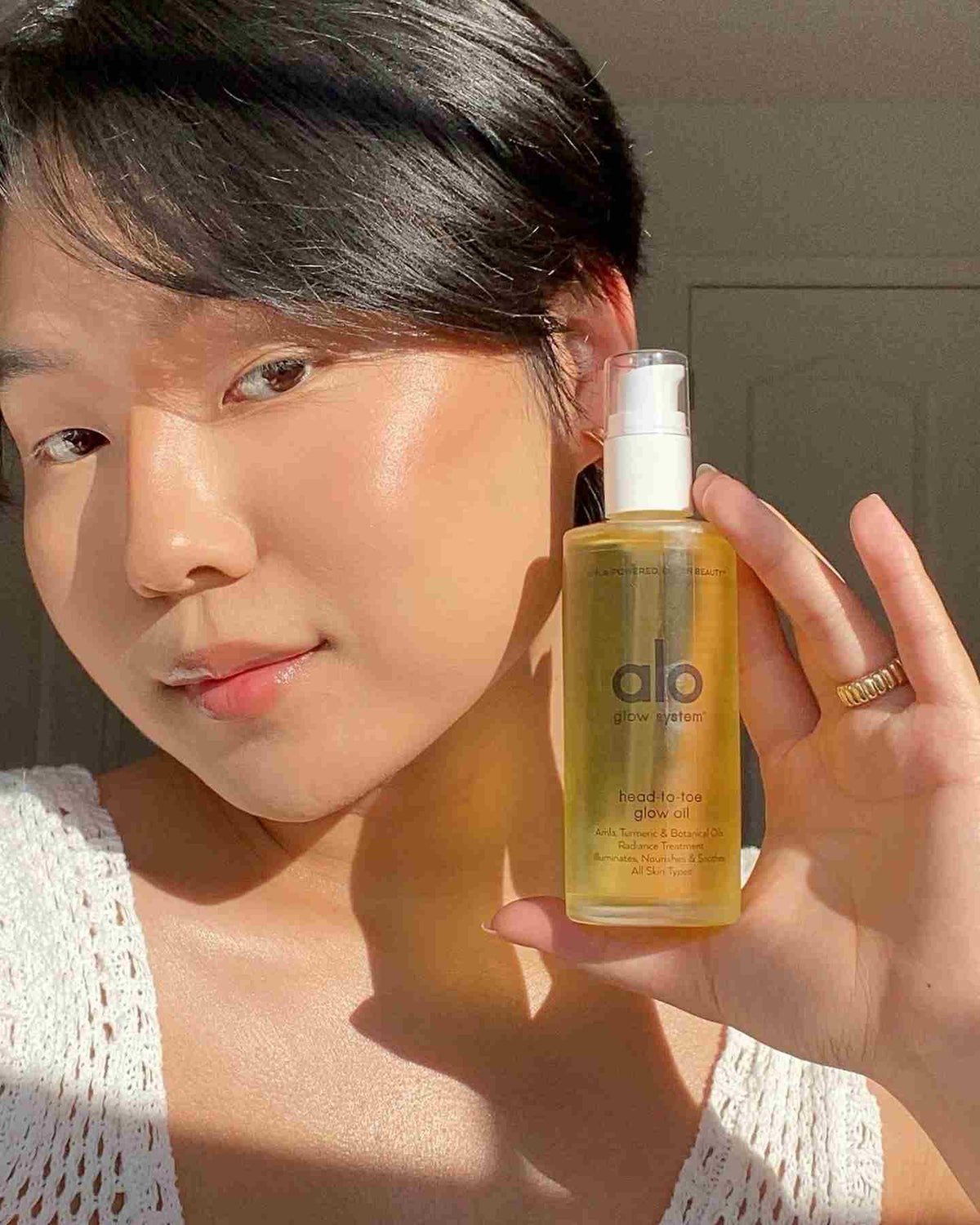 @ekunwoo holding a bottle of the Head-To-Toe Glow Oil with beautiful natural light hitting her face. 