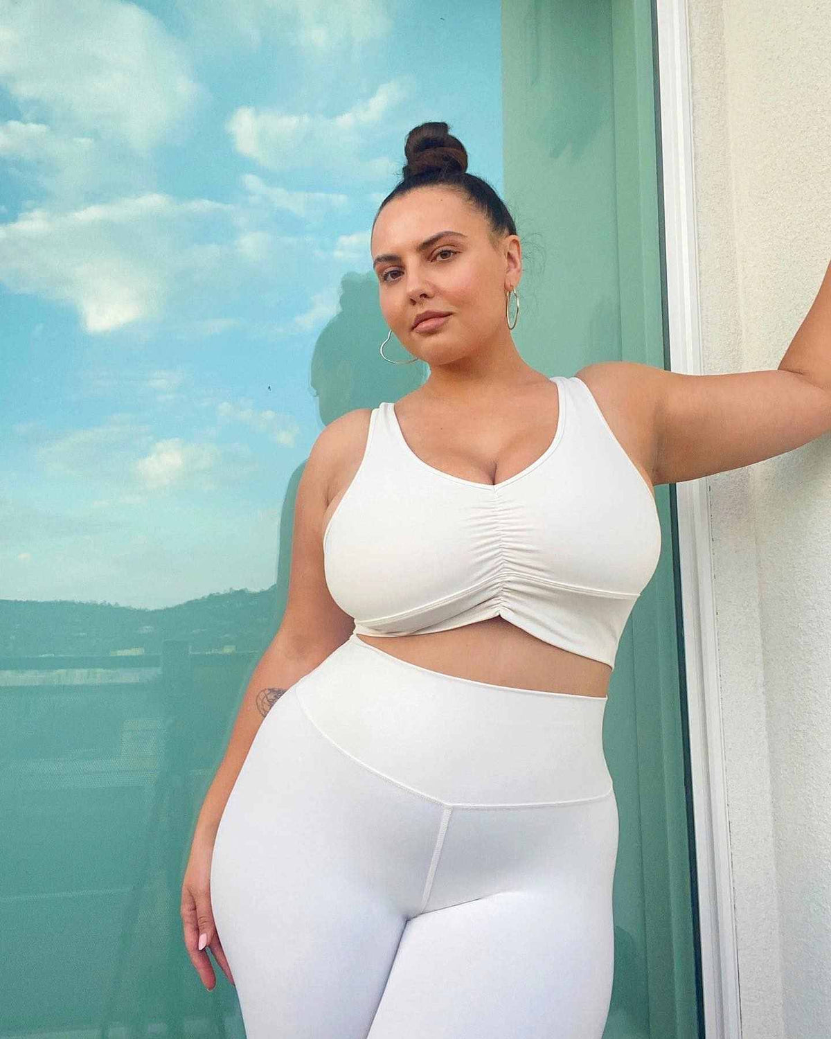 Anna Krylova wearing the Ivory Wild Thing Bra with Ivory High Waist Airbrush Leggings while posing in front of a window reflecting a blue skies and white fluffy clouds.  